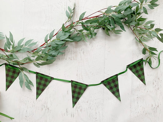 Green buffalo plaid bunting banner garland with triangular flags and a green ribbon, styled with a green eucalyptus garland on a white wood background.