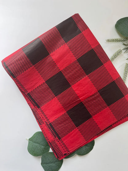 A folded red and black buffalo plaid high quality tissue paper is displayed on a clean white surface, styled with green eucalyptus leaves.