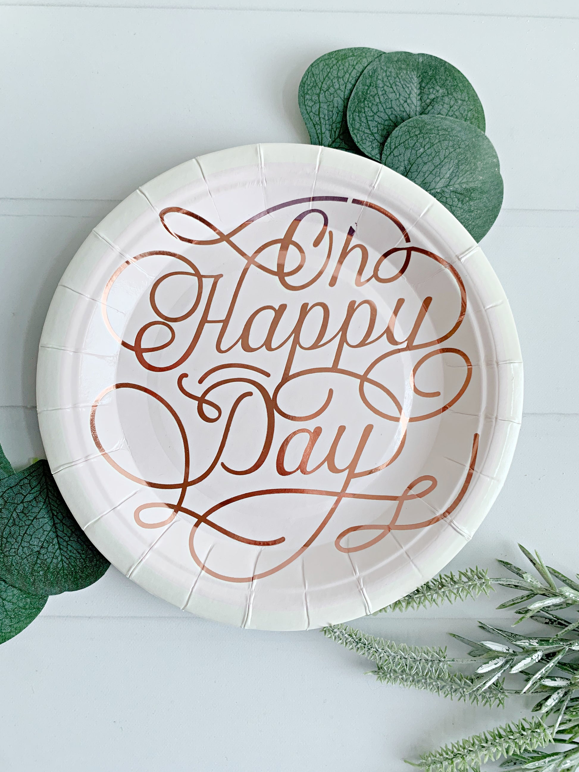 Paper plate with 'Oh Happy Day' text on a white background with greenery