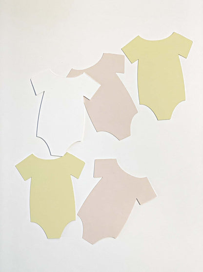 Three baby bodysuits cutouts from cardstock in pastel colors on a white background