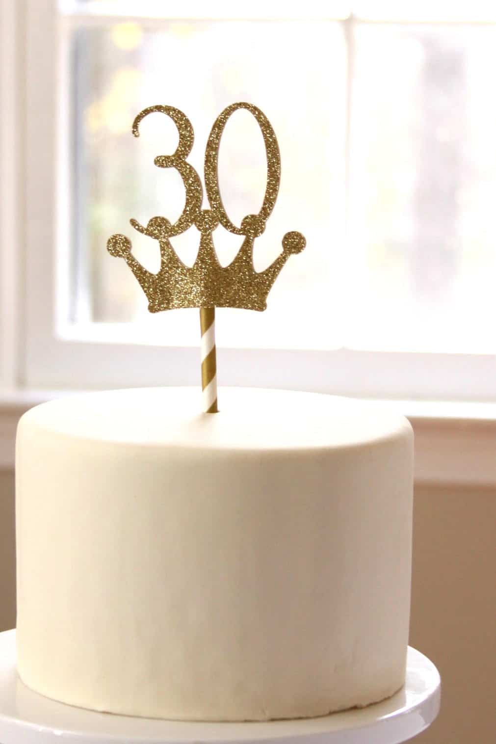 White cake with a gold '30' and crown topper on a blurred background