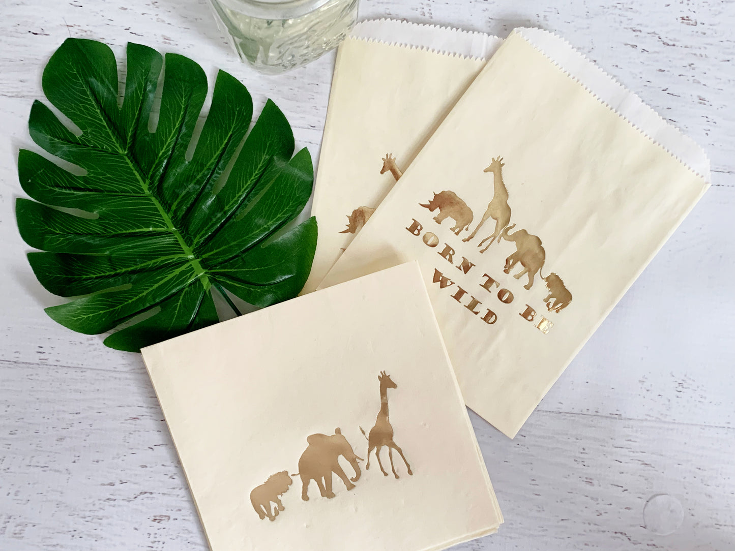 Beige pouches with animal illustrations and 'Born to be Wild' text on a white surface with a green leaf.