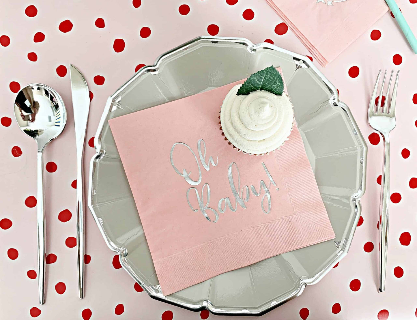 Decorative place setting with 'Oh Baby!' pink and silver napkin on a polka dot tablecloth