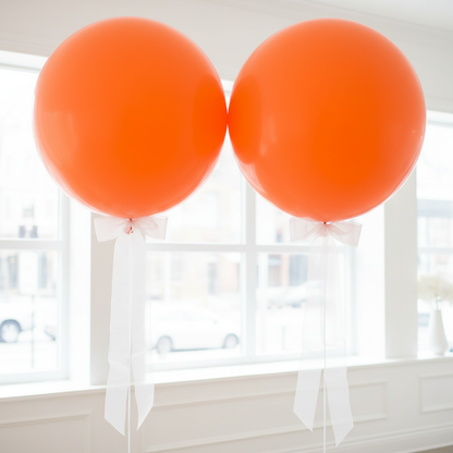Two giant orange balloons with organza bow tails